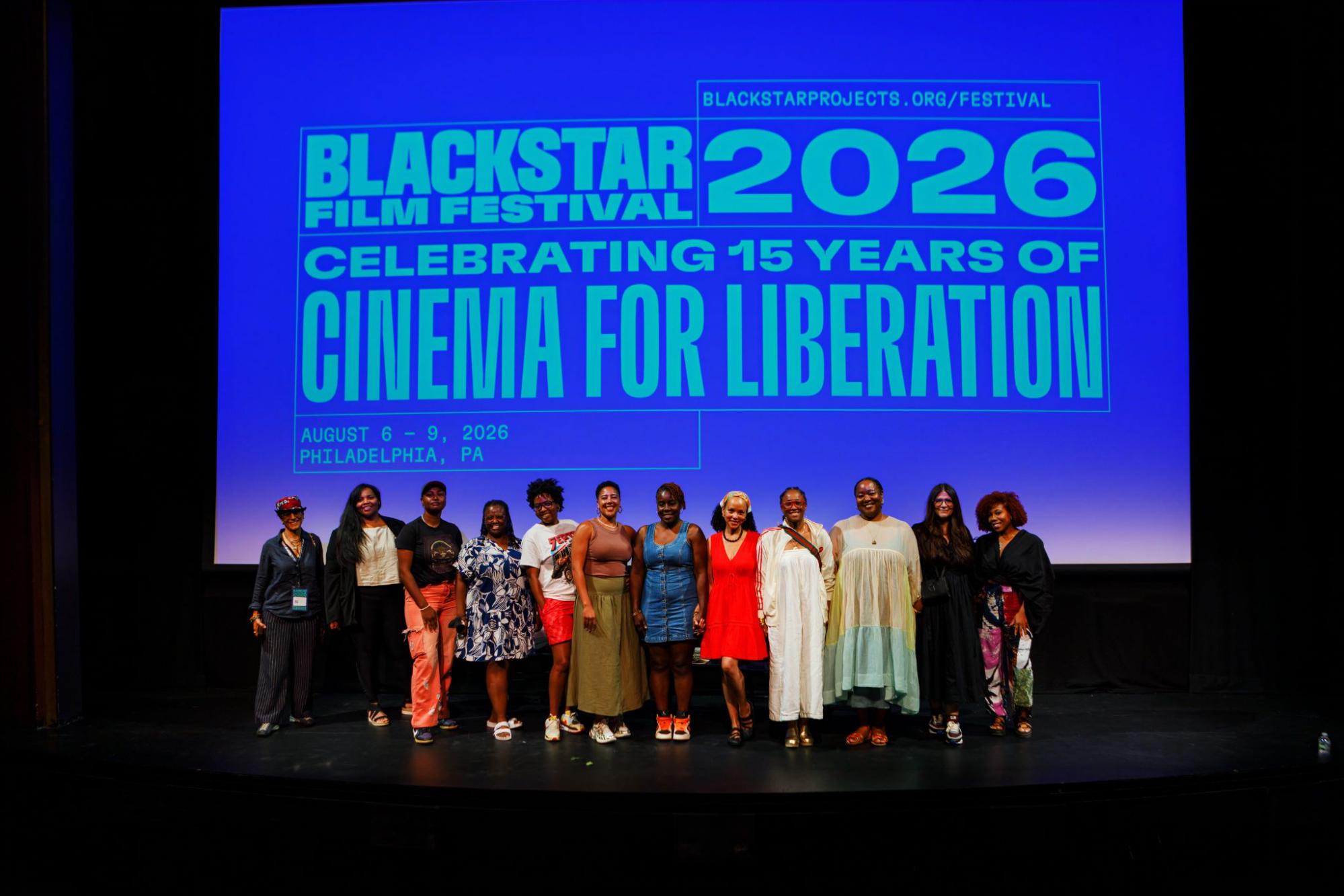 A photo of a group of people standing arm-in-arm on stage at the 2026 BlackStar Film Festival. The logo for the festival is on screen behind them.