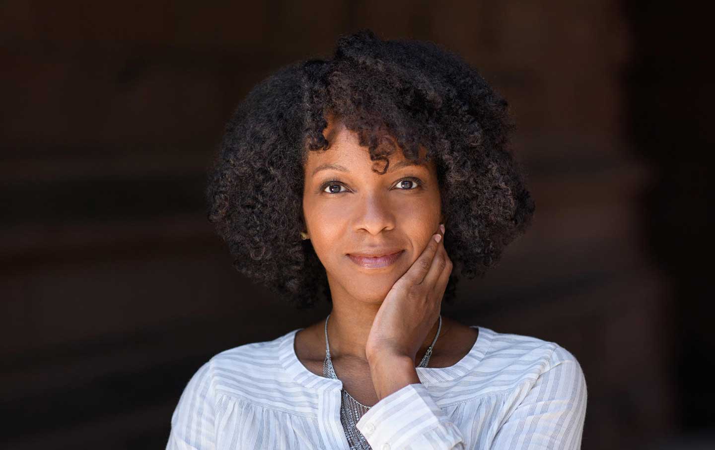 A headshot of Imani Perry. She has brown curly hair framing her face and she is looking into the camera with a slight smile.