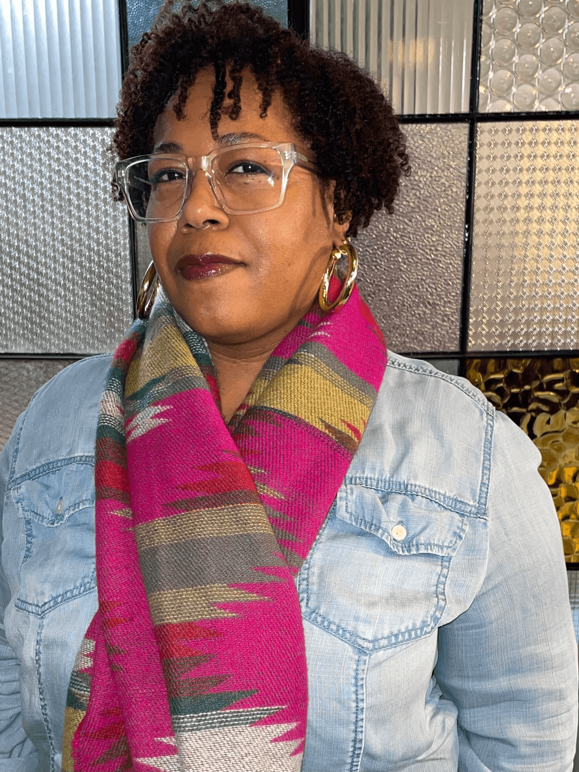 Image of Stephanie Malson shows her wearing large clear-rimmed glasses and an oversized pink scarf over a denim shirt.