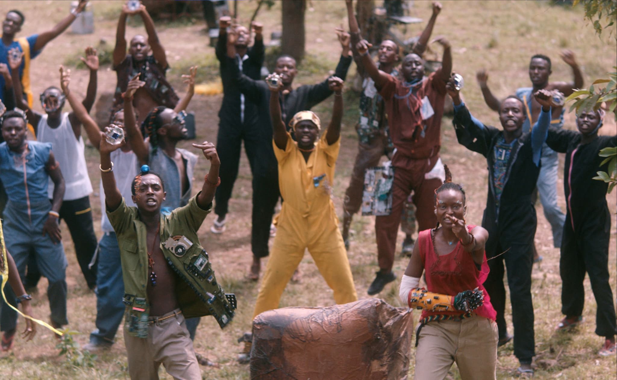 A still from Neptune Frost directed by Saul Williams. A crowd of dark skinned people raising their fists in resistance in a sandy pit.