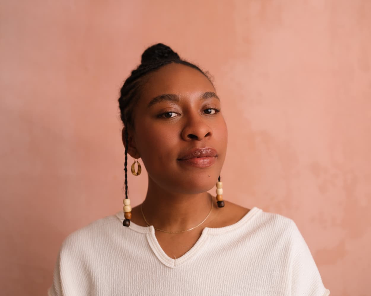 A headshot of Akua Maat. She is wearing a white shirt and in front of a salmon colored backdrop, looking directly at the camera.