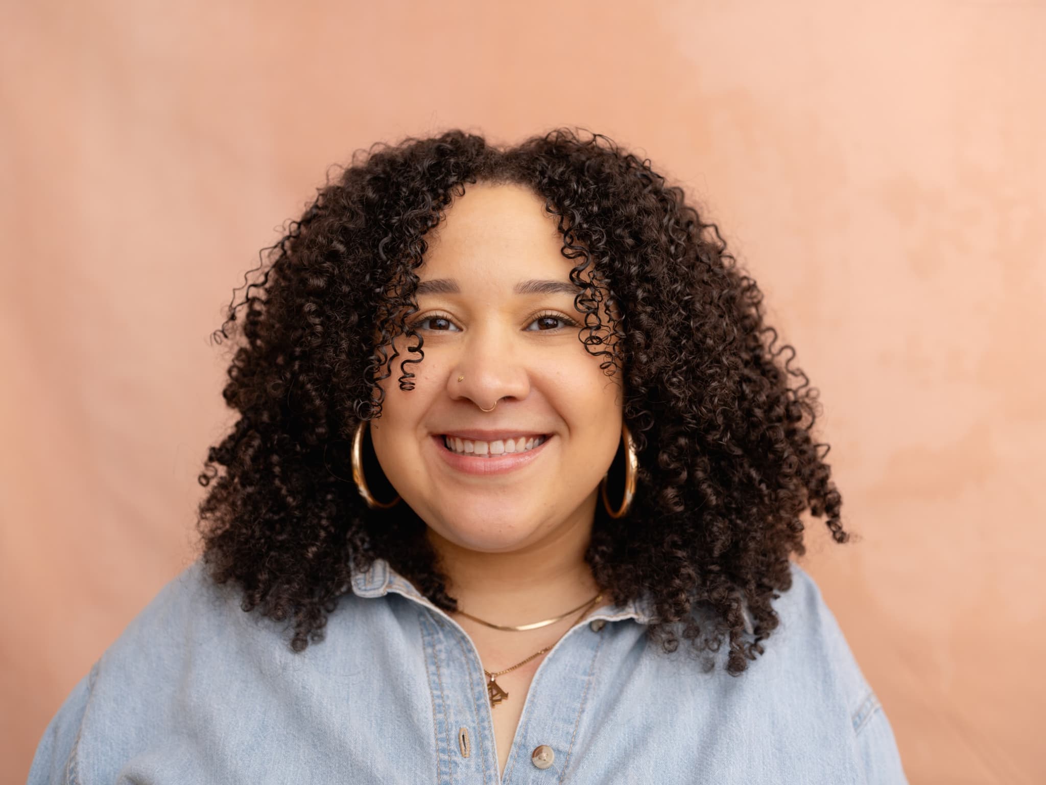 A headshot of Amber Hunnicutt, she is a Black woman. She has curly hair and is wearing gold hoops.