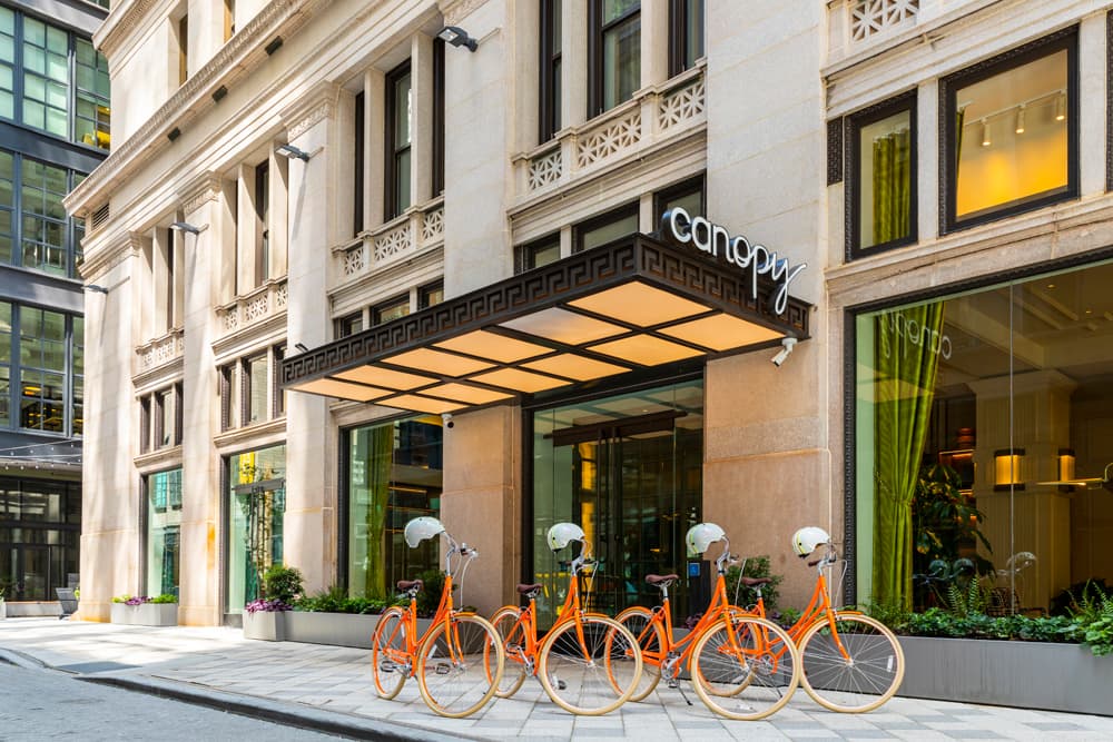 A photo of the entrance of the Canopy hotel in Philadelphia. A row of bright orange bikes are positioned in front as well.