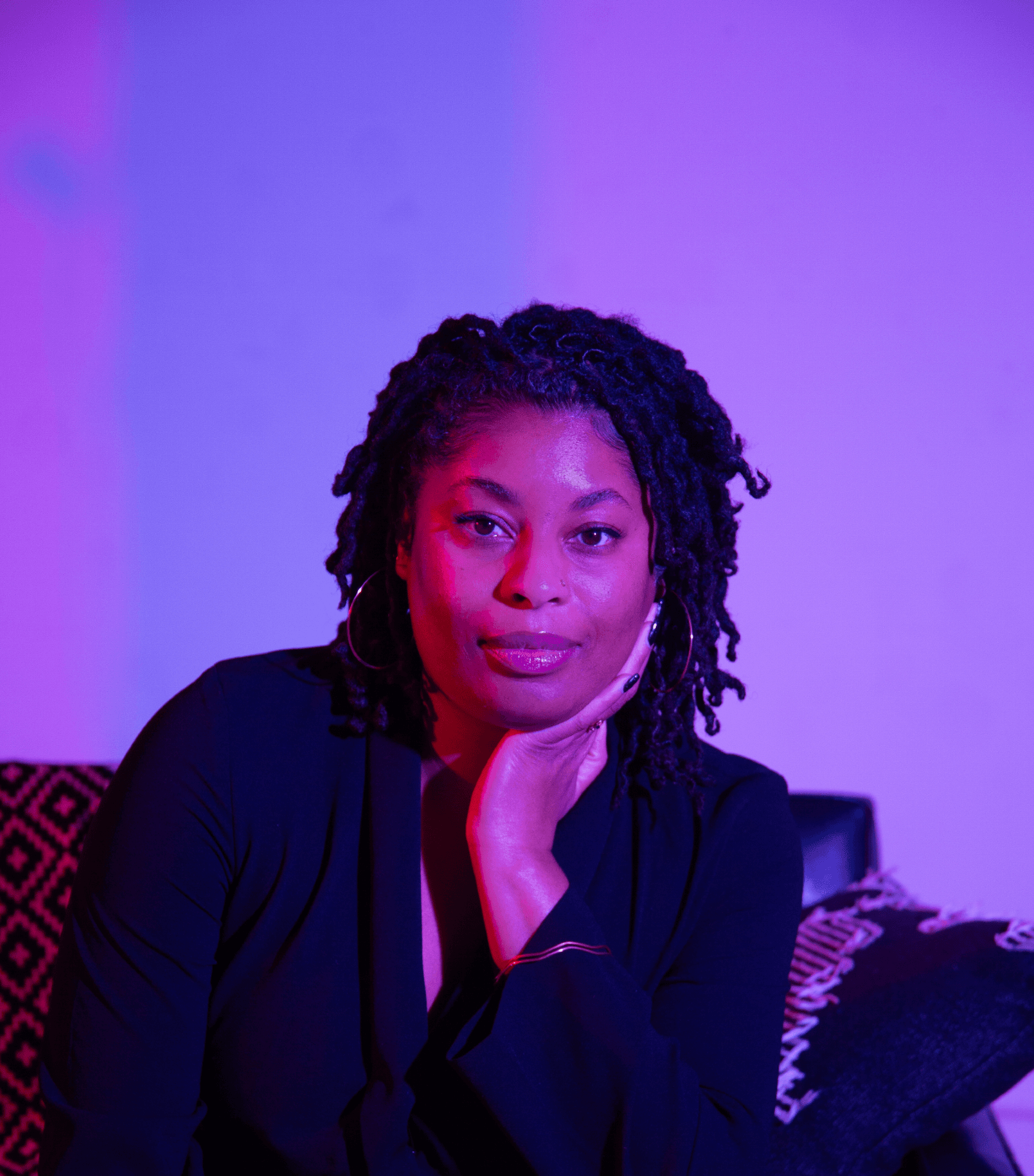 A headshot of Yasmine Espert, they are a Black non-binary person. They have locs and are smiling softly at the camera.