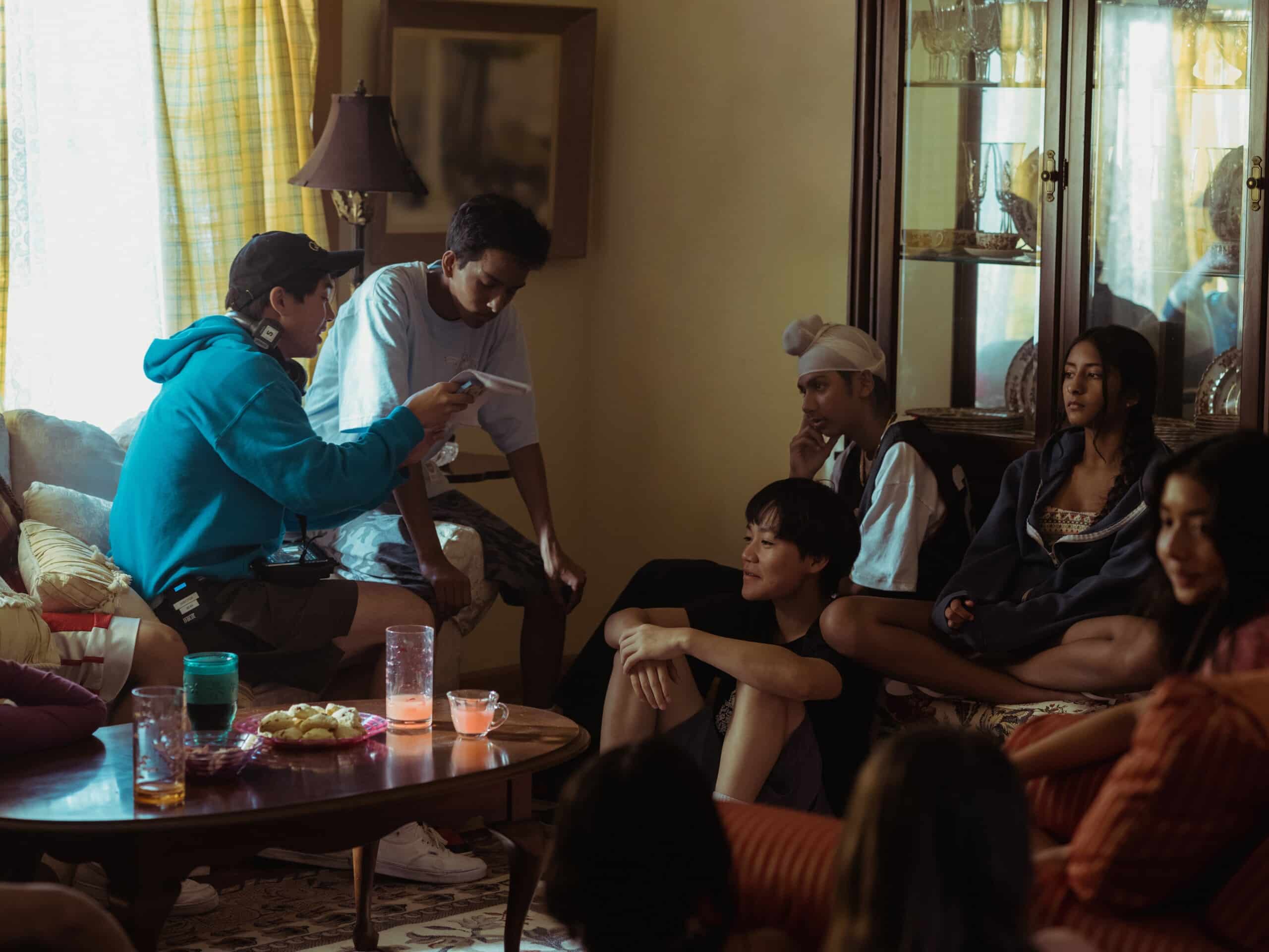 A behind the scenes shot of a group of child actors from “Didi” sitting in a living room, listening to director Sean Wang speak.