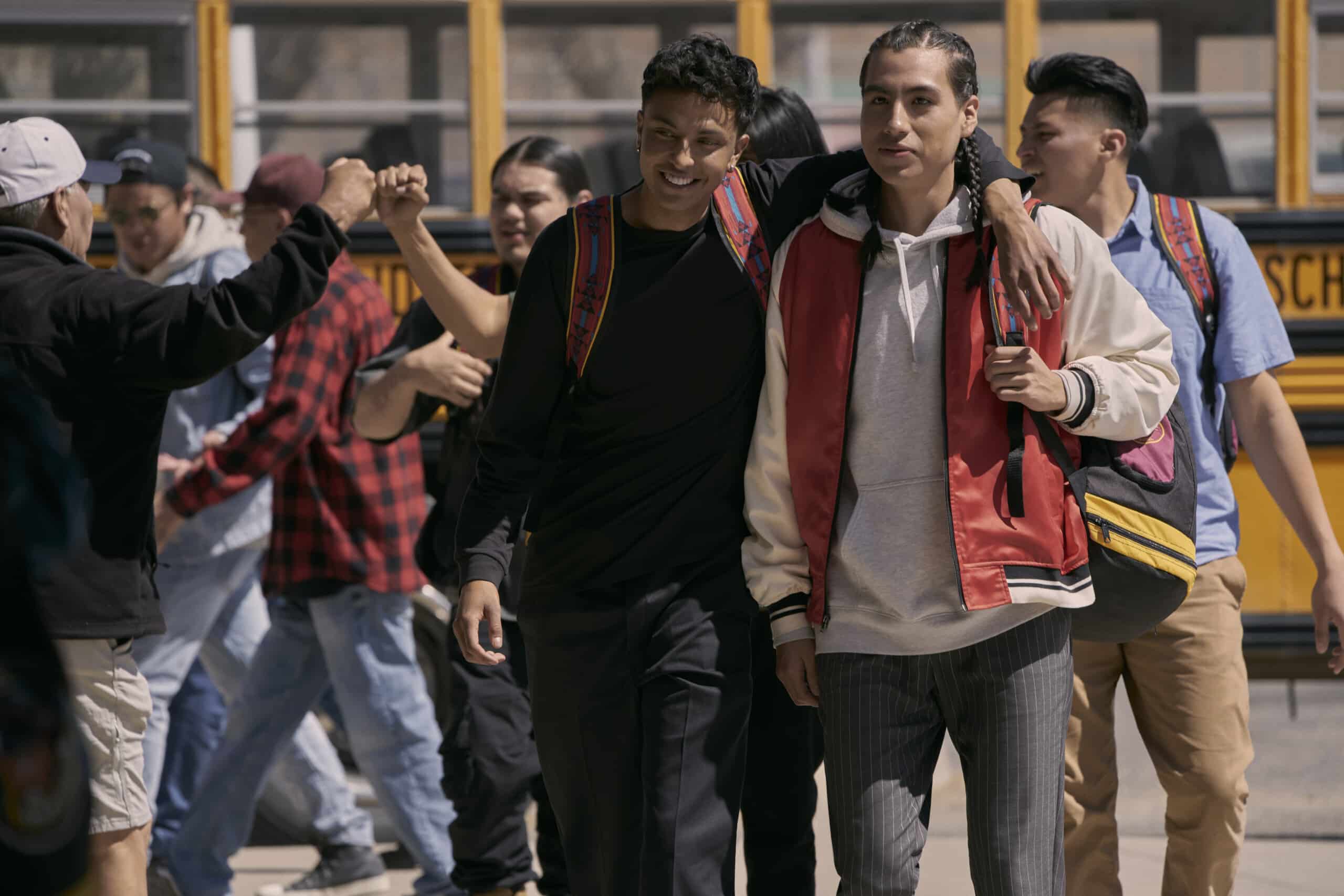 In the bottom half of the page, in a still from “Rez Ball,” Nataanii and Jimmy stand in front of a school bus with their teammates behind them.