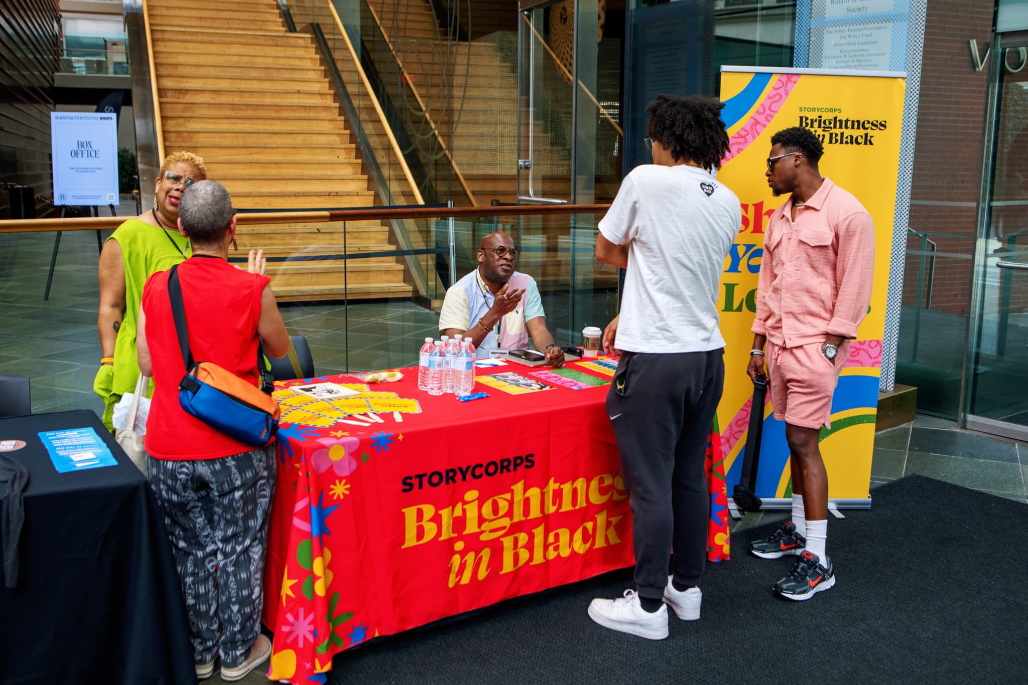 A photo from a past BlackStar Film Festival of Storycorp tabling. There are people gathered around smiling.
