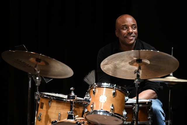 A photo of Chad Taylor. He is a Black man, he is sitting in front of a drum set.