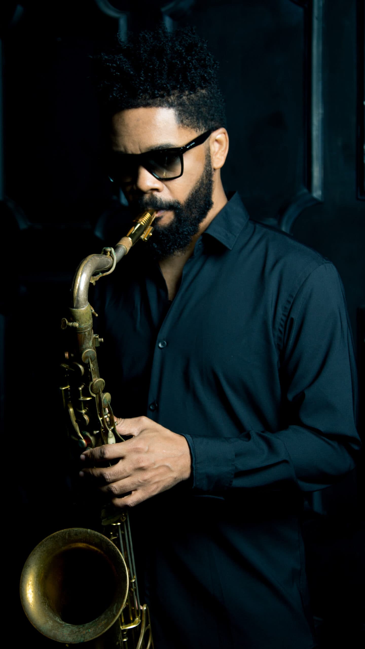 A headshot of Mark Shim. He is a Black man, he is playing the saxophone.