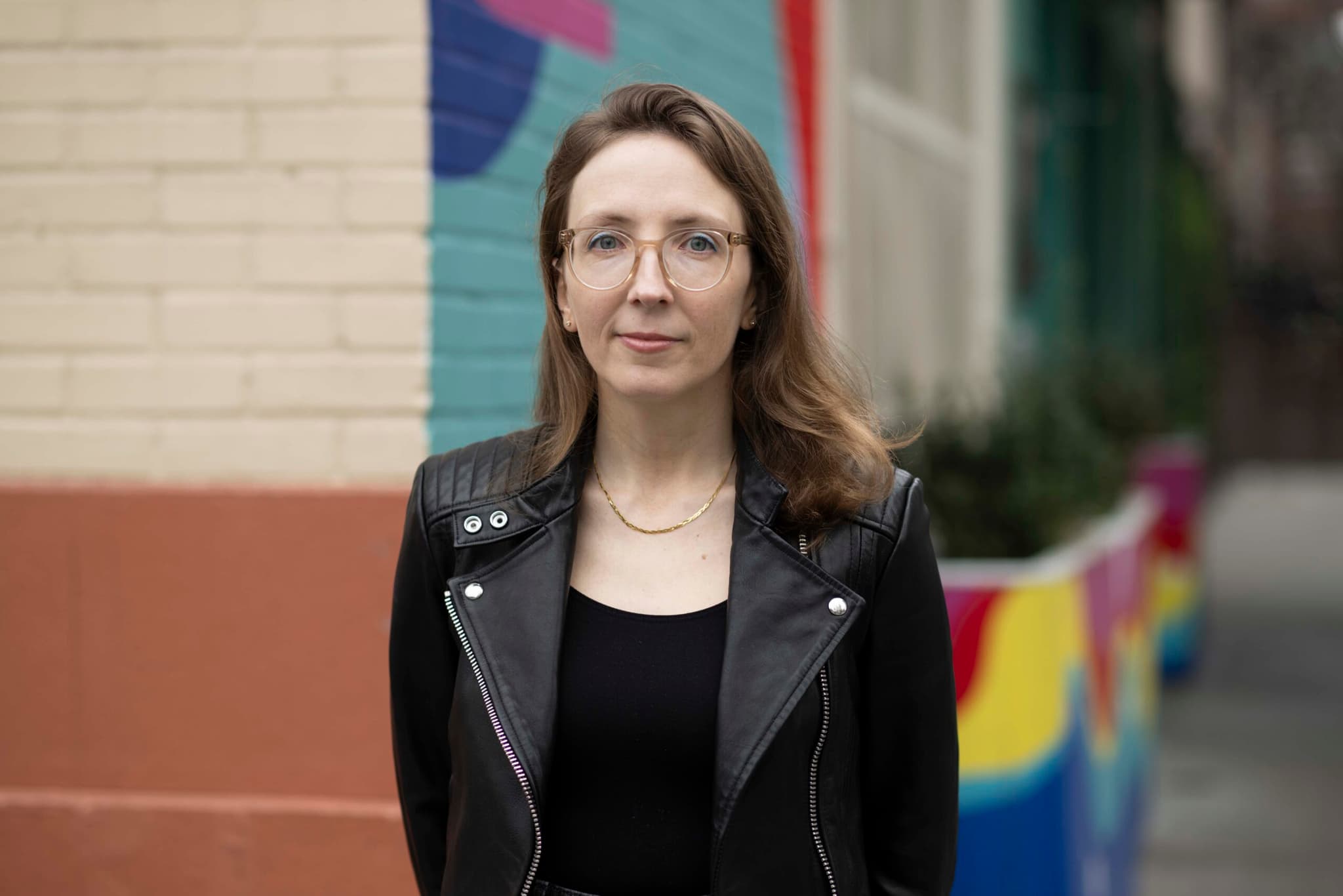 A headshot of Mary Halvorson. She is a white woman. She has long brown hair and is wearing a black leather coat.