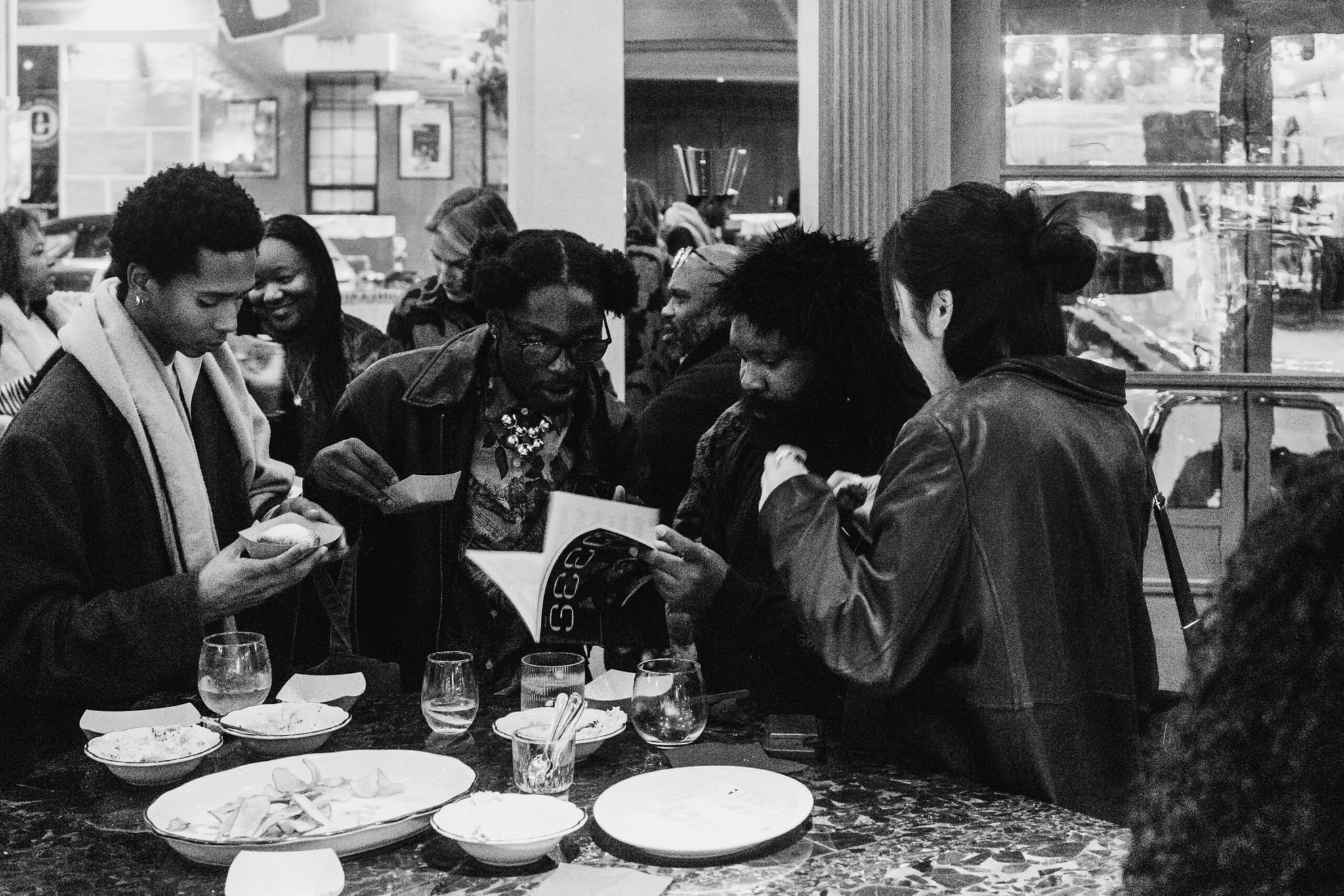 A black-and-white photo of four people at a party flipping through a copy of Seen Issue 009.