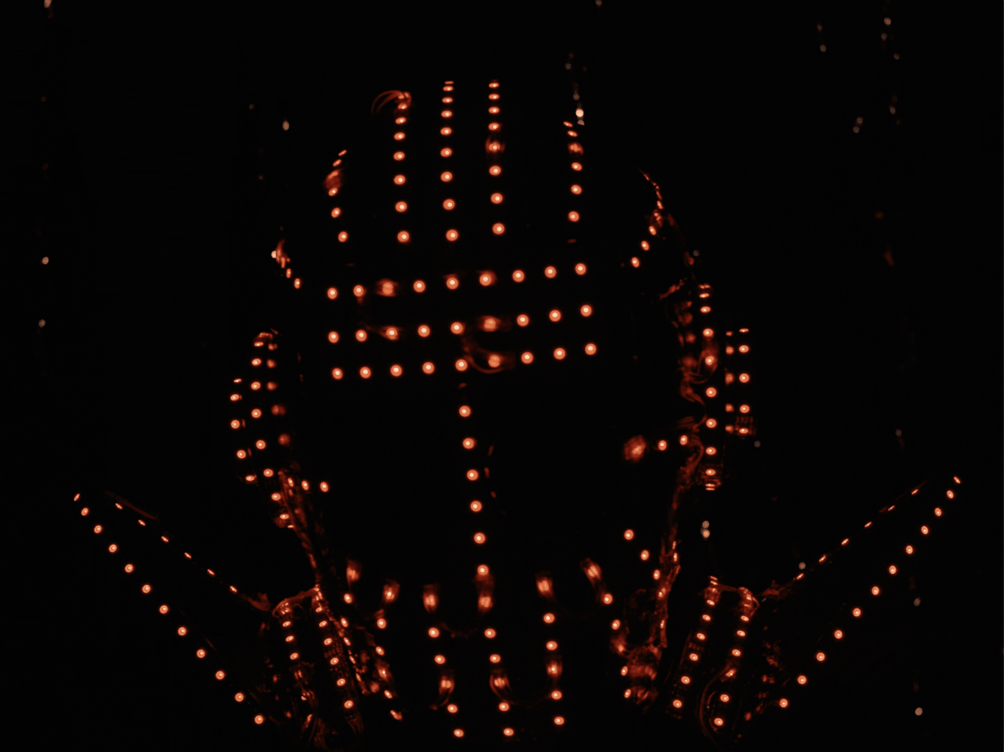Still from the film "T" shows a "soundsuit," an intricate collection of lights arranged to take the shape of a human body. In this image, the shape of a head can be seen in the dozens of orange lights.