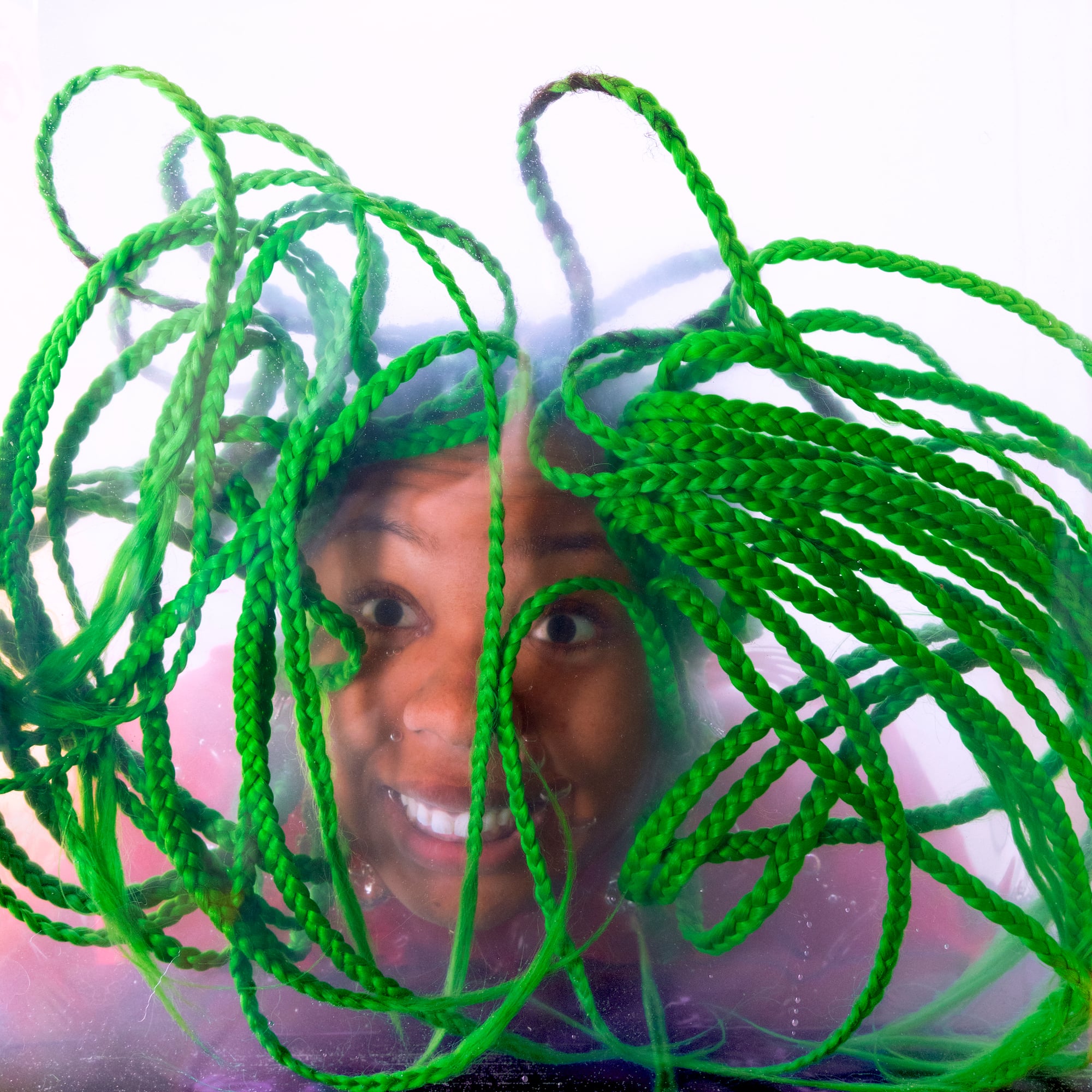 A photo of Martine Syms. Her green braids are falling in front of her face.