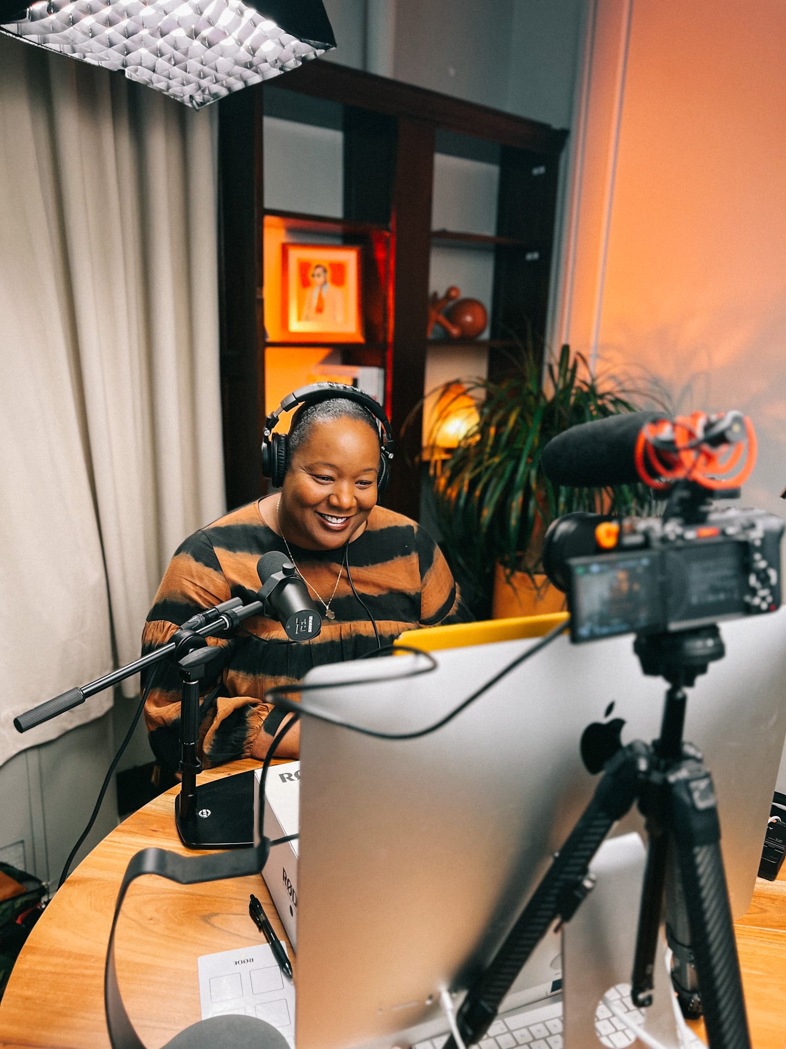 A photo of podcast host Maori Karmael Holmes speaking to someone on a computer screen, wearing headphones.