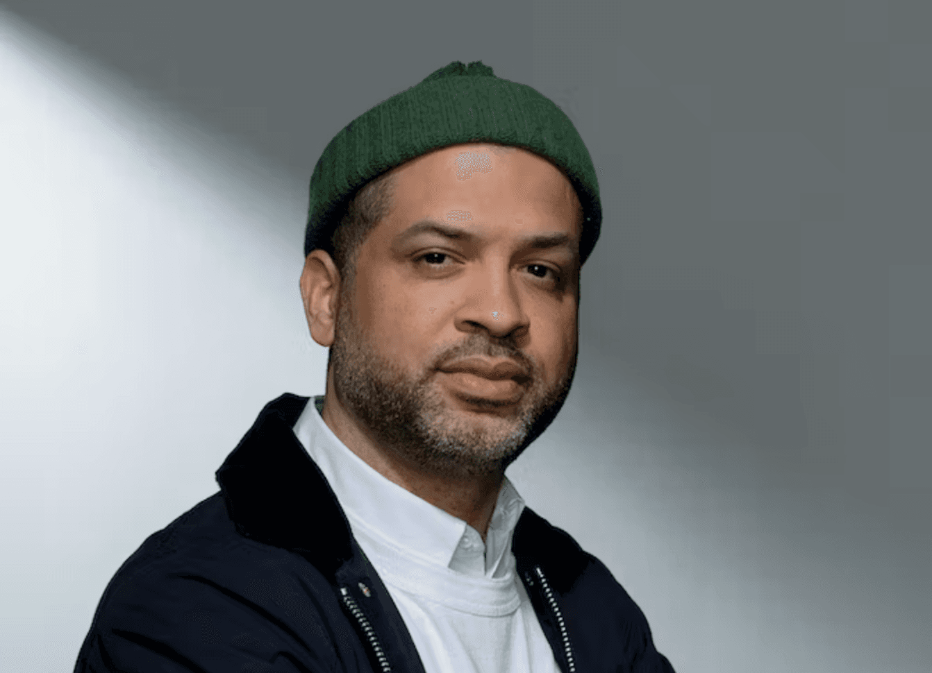A headshot of Jason Moran. He is wearing a green beanie, a white crewneck and a black jacket. He has a serious expression and is looking directly into the camera.