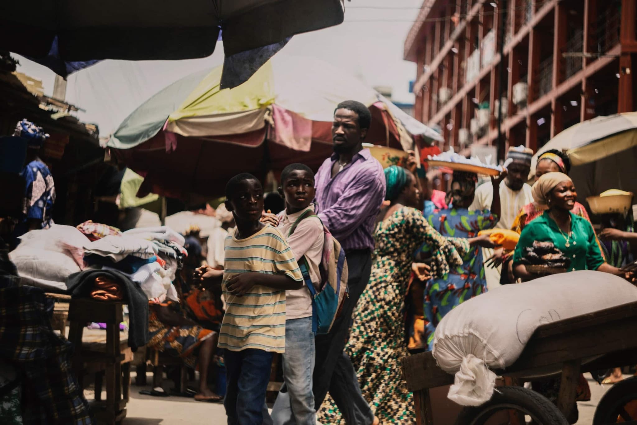 The father and his two sons are walking together down a crowded city street, holding hands as they navigate between people.