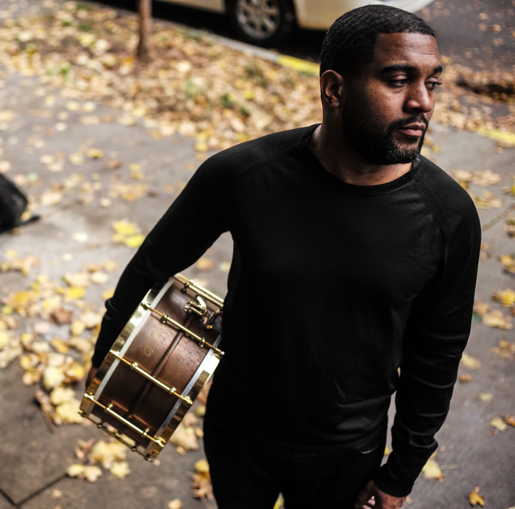 A headshot of Damion Reid. He is a Black man, he is standing with a drum in his hand.